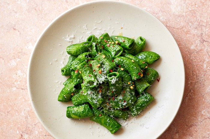 Kale pasta sauce A white plate topped with rigatoni pasta coated in a vibrant green sauce and sprinkled with chilli flakes