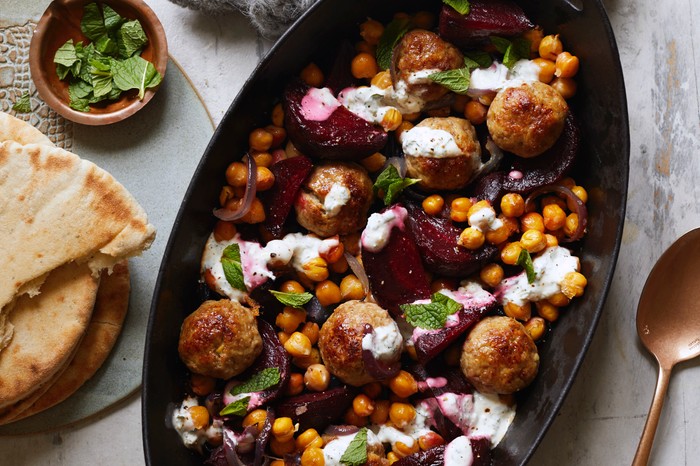 Meatball, beetroot and chickpea traybake An oval-shaped black serving bowl filled with meatballs, beetroot, chickpeas and mint