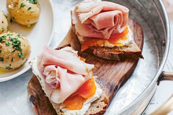 Mostarda a round metal ray with a slab of wood inside, with two pieces of bread topped with carrot and ham