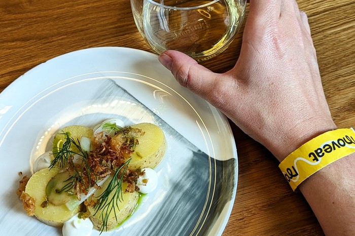 Moveat Stockholm A plate of potatoes and a glass of wine with a person's hand with a yellow Moveat wristband