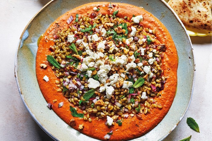 Muhammara with herby grain salad, feta and flatbreads a plate of red muhammara sauce topped with grains and herbs