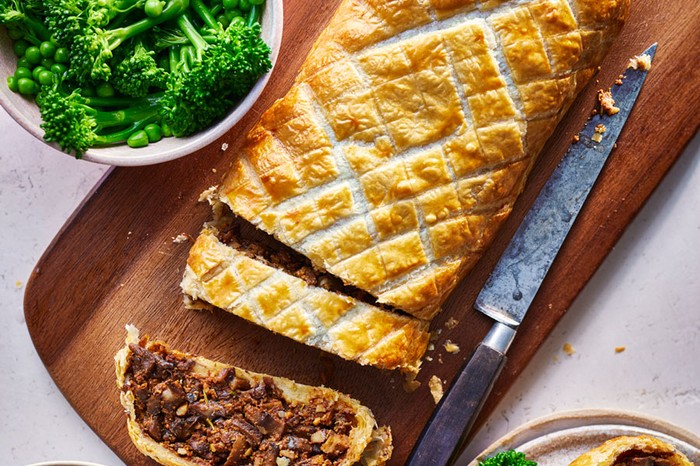 Mushroom wellington Mushroom wellington on a wooden board next to a bowl of broccoli and peas and another bowl of potatoes
