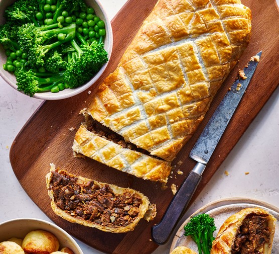 Mushroom wellington Mushroom wellington on a wooden board next to a bowl of broccoli and peas and another bowl of potatoes