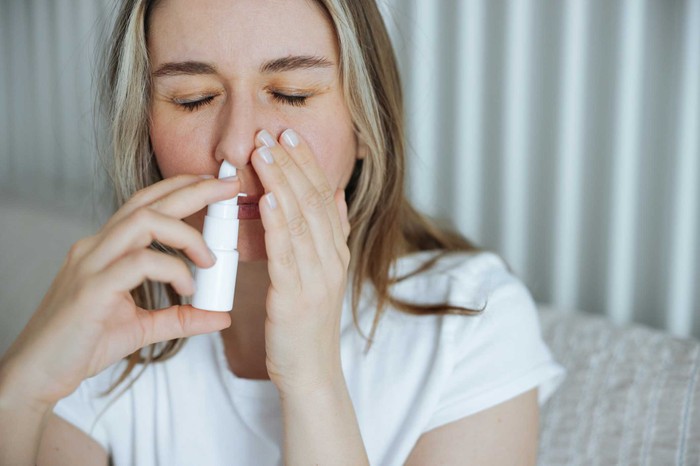 Sick young woman using nasal spray