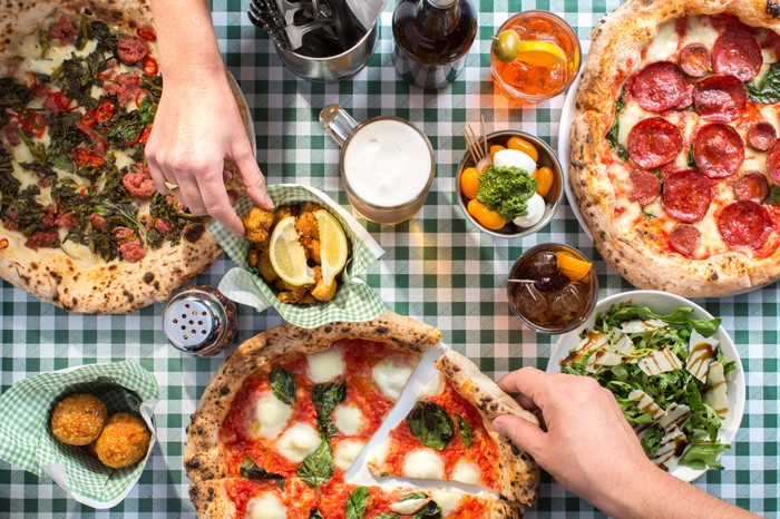 Pizza Pilgrims Two different hands reaching across the table for food, with three different Naples-style pizza, salad and drinks