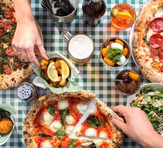25 best pizza places in London Two different hands reaching across the table for food, with three different Naples-style pizza, salad and drinks