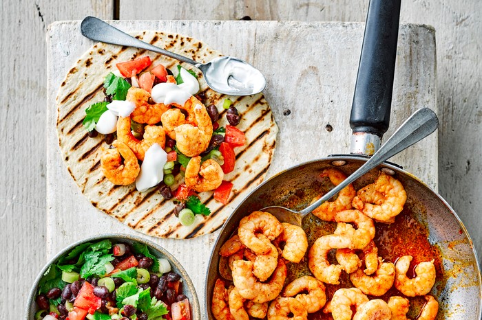 Prawn tacos next to a pan of prawns and bowl of chopped tomato and coriander salad