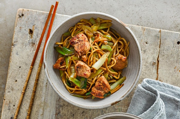 Chicken chow mein A bowl of chicken chow mein on a grey serving board next to chopsticks