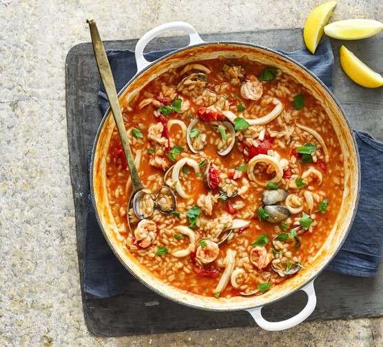 Perfect seafood risotto Seafood risotto in a large pot with a serving spoon, next to a wedge of lemon