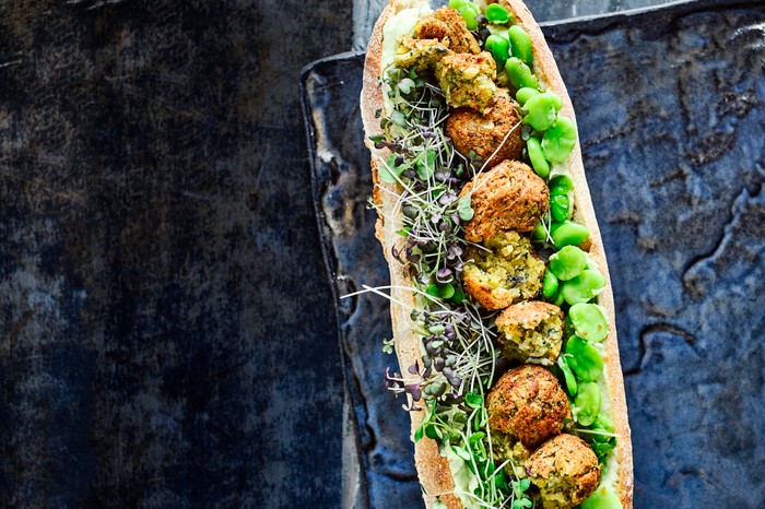 Falafel with Avocado Hummus Recipe and Broad Beans Falafel with Avocado Hummus Recipe and Broad Beans served in a crispy white baguette on a dark blue tray and table
