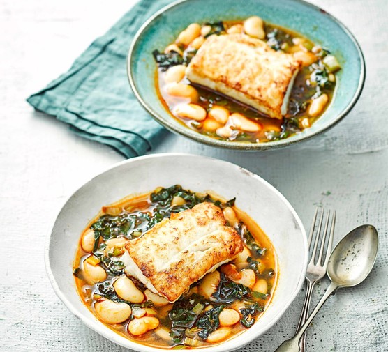 Pan fried cod with giant beans and chard Two plates of pan fried cod, served with giant butter beans and chard, next to a fork and spoon.
