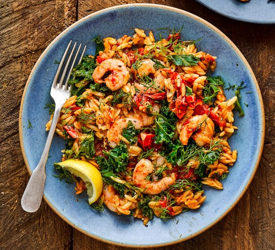 Baked orzo with harissa prawns on a blue plate with a wedge of lemon and fork
