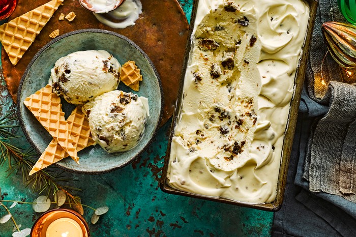 A tub of homemade ice cream with a plate of ice cream scoops and wafers on the side