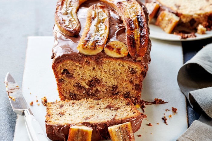 banana and chocolate cake with caramelised bananas A banana and chocolate chip loaf cake on a white serving board, with a slice cut from the end