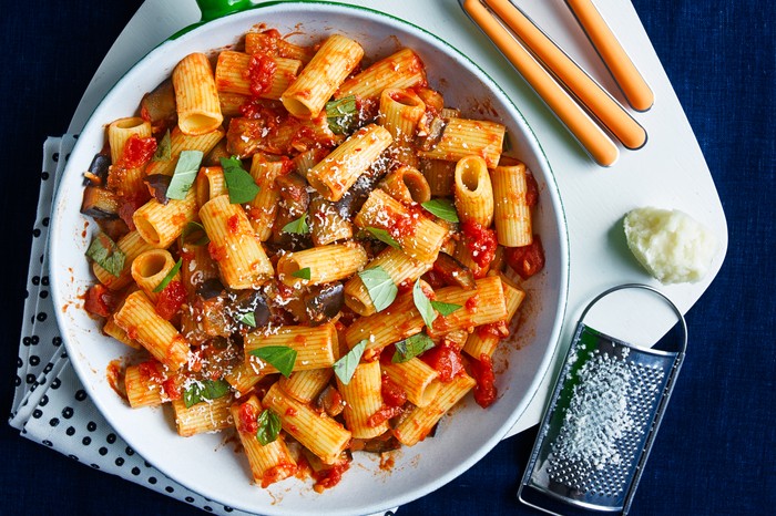 Pasta norma in a pan next to two sets of spoons and forks