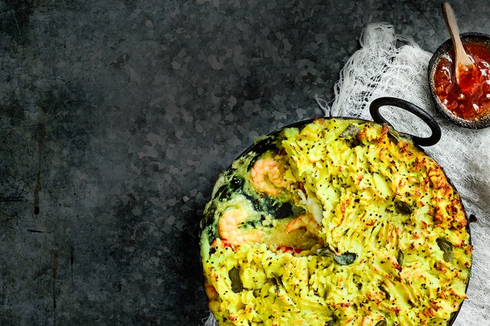 Indian Fish Pie Recipe Indian Fish Pie Recipe served in a black round oven proof dish with a small dish of mango chutney on the side