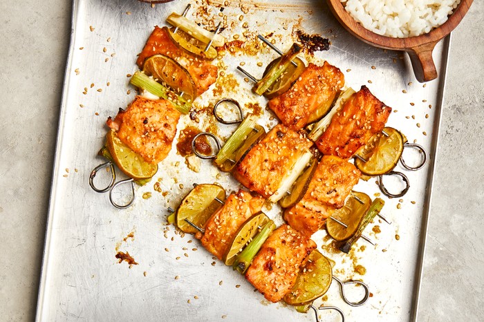 Umeboshi salmon skewers A metal tray topped with skewers pierced with chunks of salmon with spring onions and lime