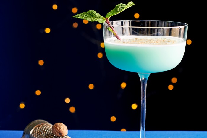 A blue cocktail garnished with a sprig of green mint