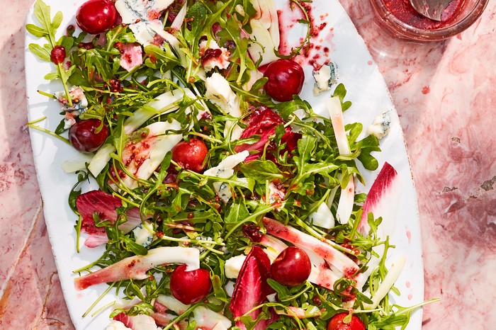 Pickled cherry, gorgonzola and rocket salad A white oval platter on pink mottled stone, topped with rocket leaves and cherries