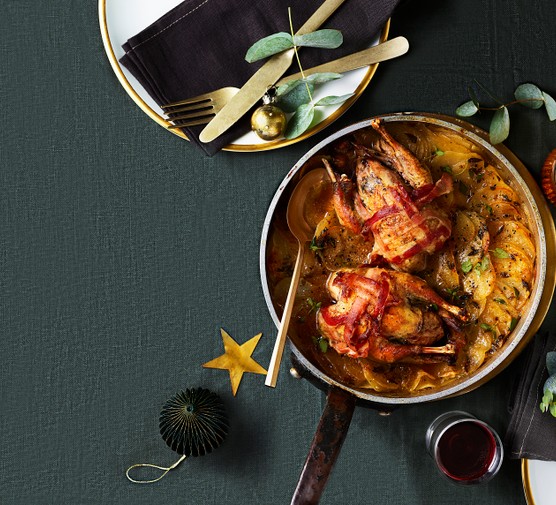 Roast partridge with one-pan boulangère A bowl filled with two roast partridges topped with crispy bacon with layered potatoes underneath