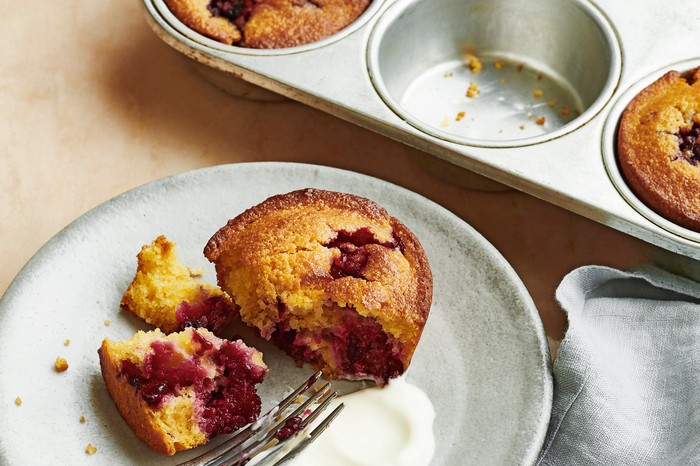 A broken muffin on a stoneware plate next to a fork and a muffin tin
