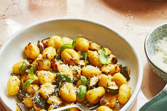 Courgette, brown butter and basil gnocchi Two bowls of gnocchi on a table garnished with basil and grated cheese