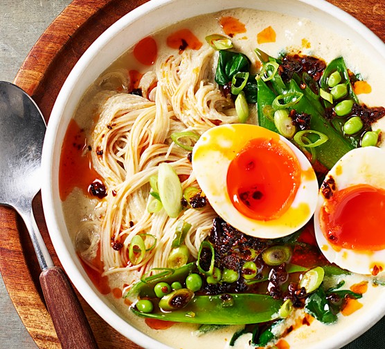 Miso tofu soup Two white bowls filled with noodles, green vegetable and eggs with a bright orange yolk