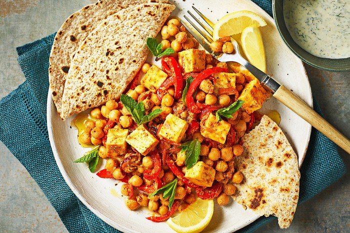 Paneer and chickpea curry A white plate topped with a chickpea and paneer curry with two chapatis on the side