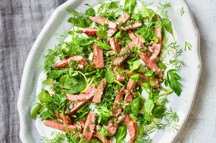 Roast Lamb Salad with Mint Dressing A white platter with green leaves and slices of pink lamb