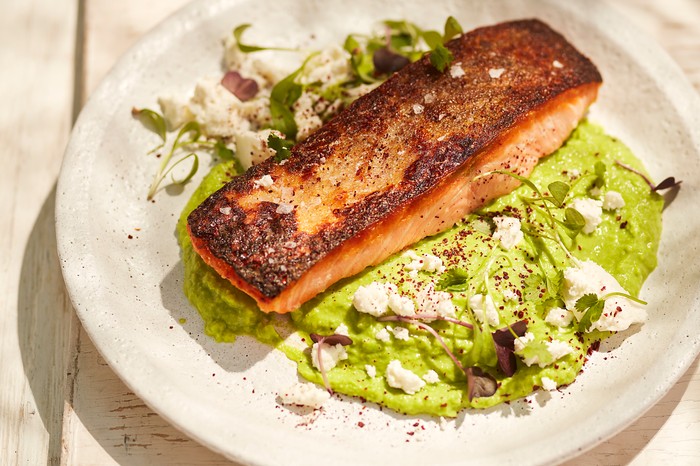 Seared Salmon with Pea Purée A fillet of salmon sat on a bed of green purée in the sun on cream plate