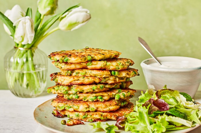 Pea and halloumi fritters with charred lemon dip Stack of pea and halloumi fritters next to a salad
