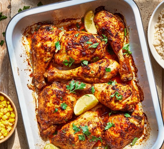 Peri peri chicken traybake a silver oven tray filed with chicken topped with chopped herbs and lemon wedges