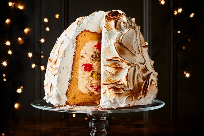 A Pistachio and cherry nougat cheesecake-stuffed pandoro on a cake stand with a black background