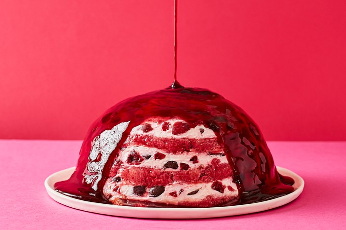 Cherry labneh summer pudding A round cherry pudding with sauce being spooned over the top
