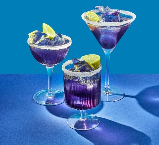 Purple rain Three different shaped cocktail glasses filled with a purple drink, ice cubes and lime wedges on a blue background
