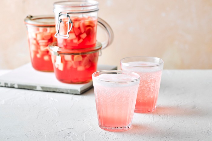 Rhubarb Gin Recipe Rhubarb gin and tonic in a glass with a jar of rhubarb behind