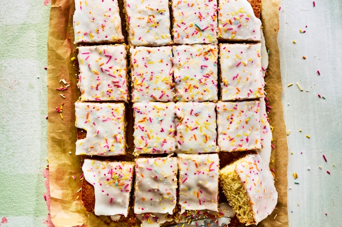School cake A school cake topped with icing and sprinkles cut into squares on a sheet of brown baking parchment