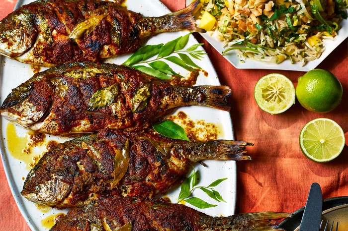 bbq masala fish with a rice, mango and coconut salad Barbecued fish on a platter with a side salad, laid out on an orange tablecloth