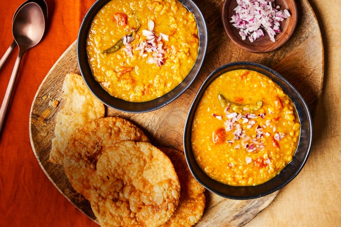 Sindhi dhal pakwan Two bowls of dhal next to a pile of pakwan bread and a ramekin of chopped onions