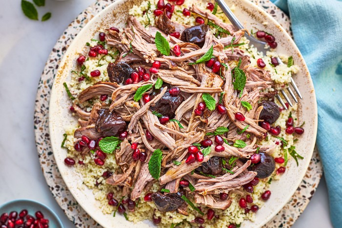 Slow cooker leg of lamb Plate of shredded leg of lamb topped with prunes, pomegranate seeds and mint