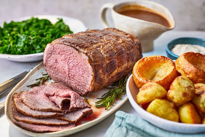 Slow-cooker roast beef Sliced roast beef next to roast potatoes, yorkshire puddings and greens