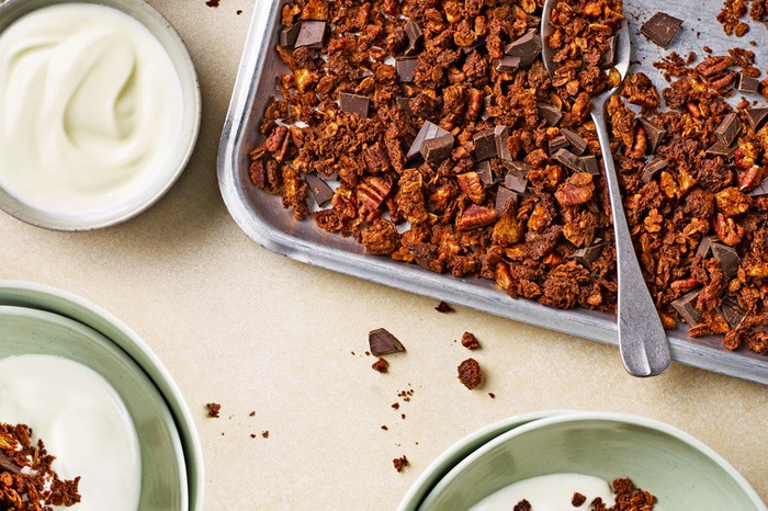 Sourdough-chocolate-granola Baking tray of sourdough chocolate granola next to a bowl of yoghurt and two bowls of granola and yoghurt