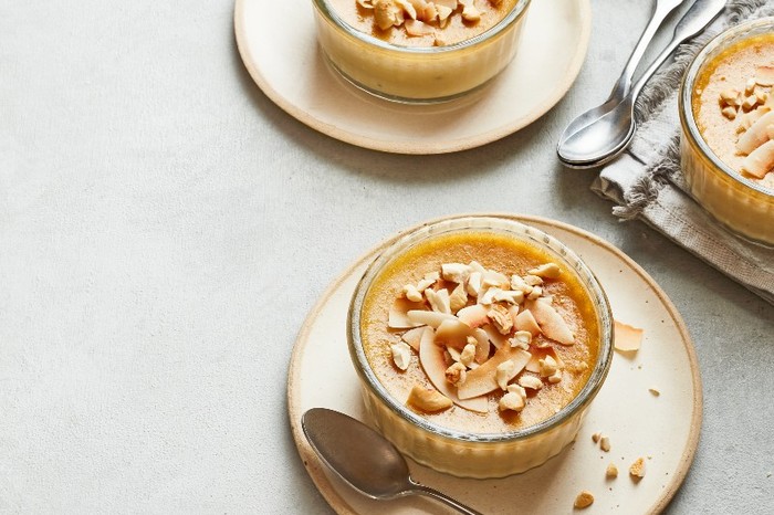 Sri Lankan watalappan coconut custard with kithul glass ramekins on stone plates filled with a set custard and topped with coconut flakes
