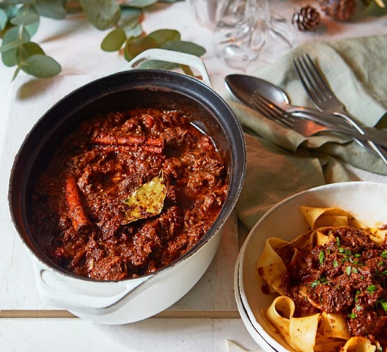 Stifado An ovenproof pot filled with stifado stew, next to a bowl of pasta with the stew piled on top