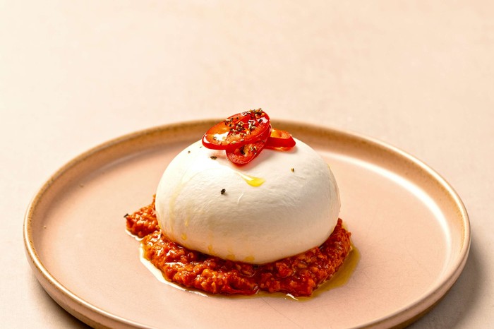 Burrata, romesco and red chilli A whole burrata ball on a small serving plate with romesco pepper underneath it and on top