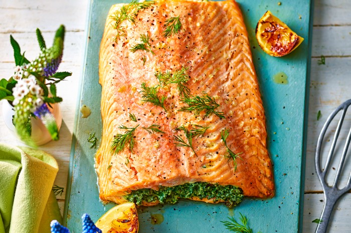 stuffed salmon side with creamy spinach salmon stuffed with a green herby mixture and topped with dill fronds on a blue chopping board with a green napkin