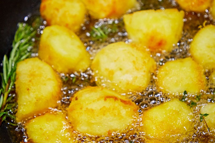 Beef dripping roast potatoes Potatoes roasting in fat in a tin with thyme on the side
