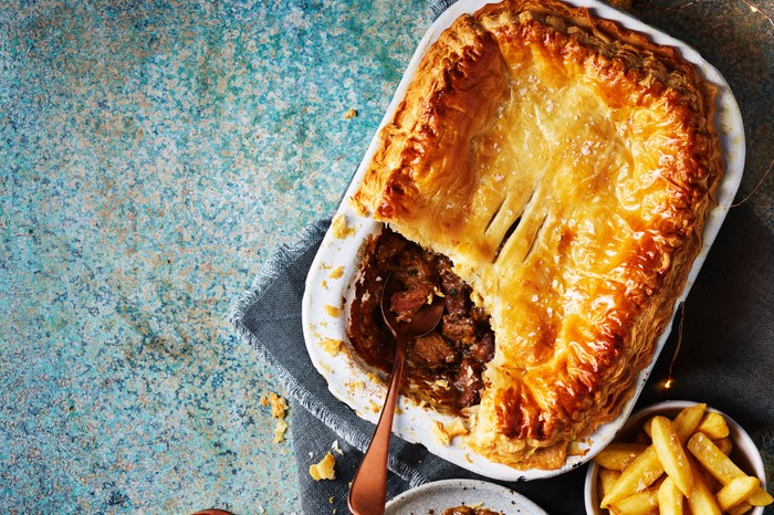 A rectangular steak pie cut open with a small bowl of chips on the side