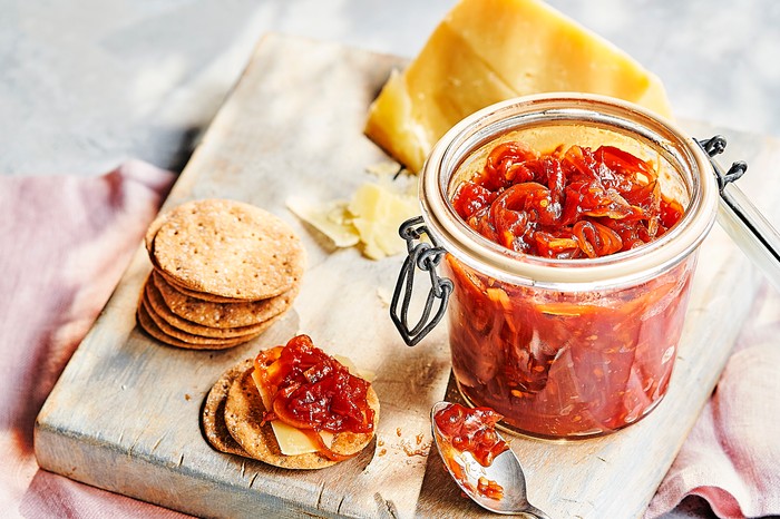 Tomato chutney a jar of red tomato chutney on a wooden board with round crackers and a block of cheese