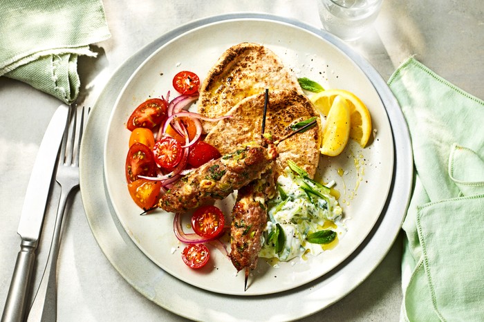 Turkey and Feta Kebabs A plate on a white background with green napkins, filled with turkey skewers and charred pitta breads